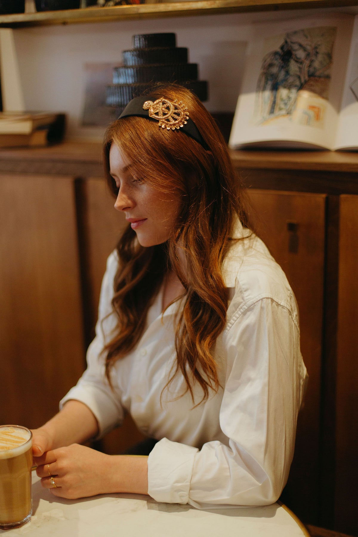 Serre tête Ella bleu nuit porté avec chemise blanche dans un café 